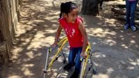 Wiliany, 7 years old, in Zulia State, Venezuela, in March 2022.  Photo showing Wiliany, leaning on her walking frame and smiling.