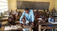 Yao Gbledjo during a support session in an inclusive class In a full classroom, Yao leans over a child to help him.