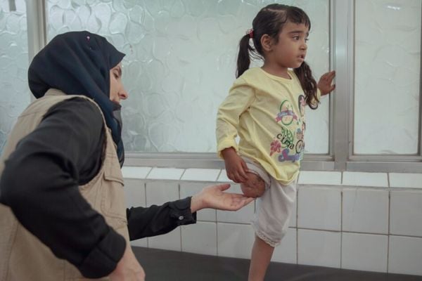 A girl amputee stands on one leg as an HI physiotherapist assesses her, Yemen.