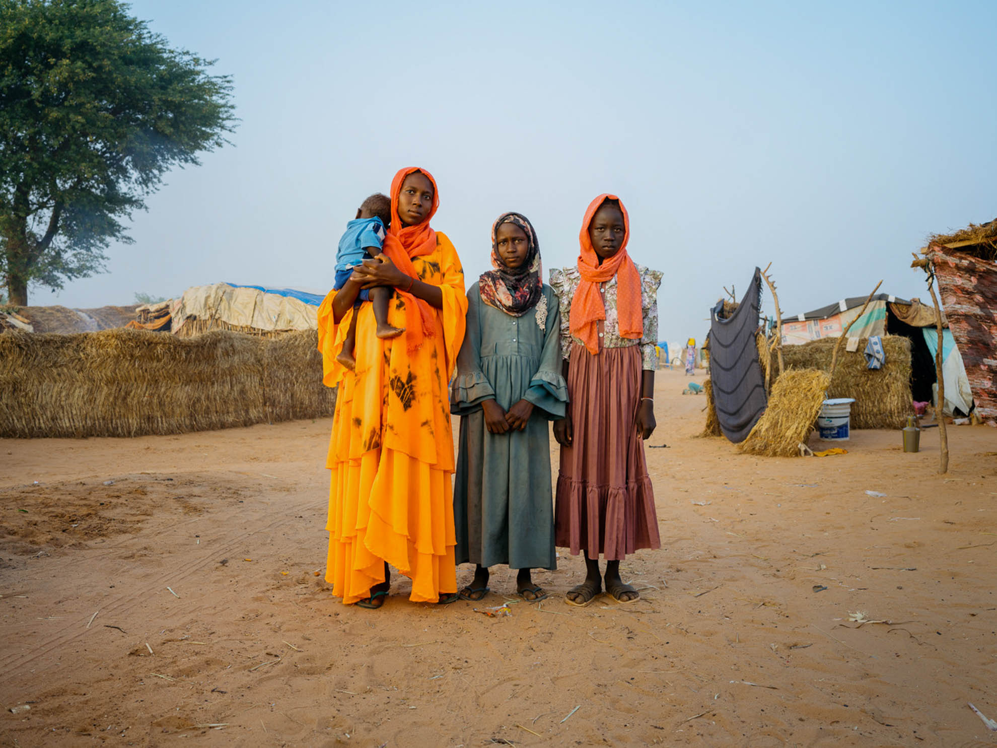 Sisters Aman who is holding a baby and Fatna with their cousin Mukhtadar standing in the middle of the camp